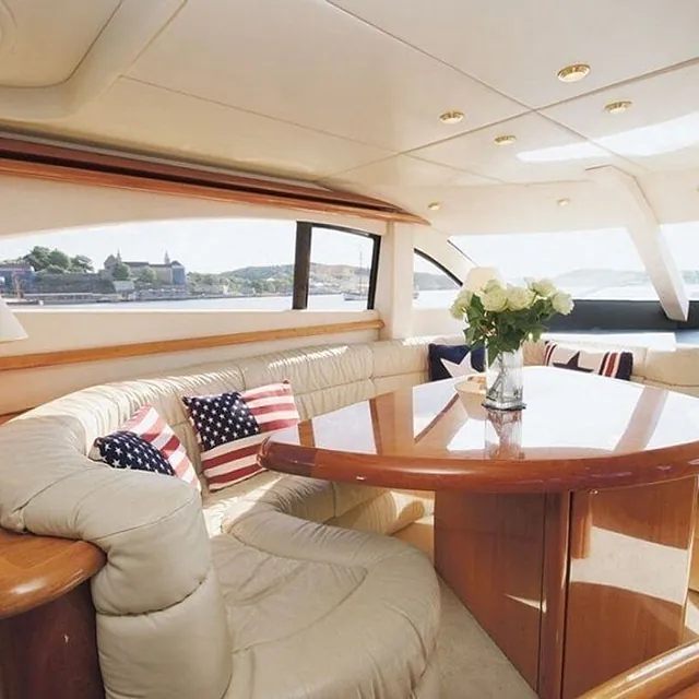 Lys salong med buet sofa, spisebord og store vinduer med utsikt over sjøen.