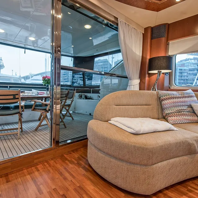 Nærbilde av sofahjørne ved skyvedør til dekk, med utsikt til marina og andre båter