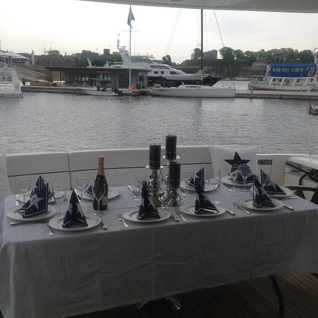 Dekket dekket til fest med hvit duk, stettglass og pynt, med marina i bakgrunnen.