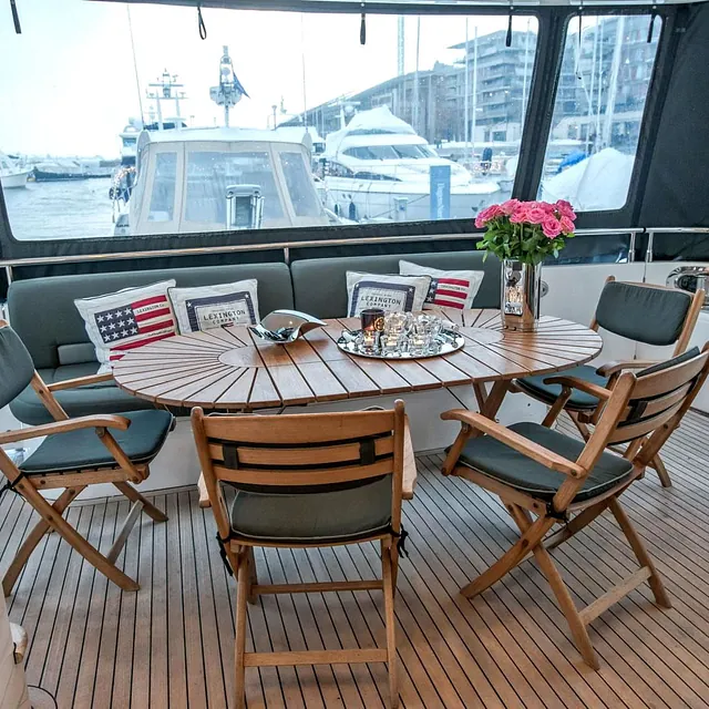 Uteplass på yacht med rundt trebord, seks stoler og pynteputer med amerikansk motiv