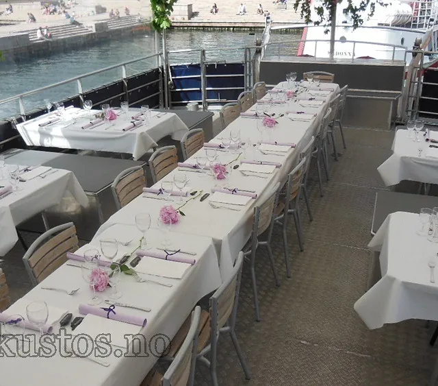 Pent dekket langbord med hvite duker og blomsterdekor på båtens utendørsdekk.