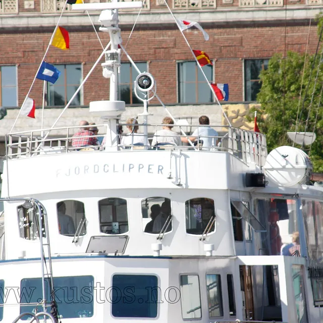 Folk sitter på øvre dekk av Fjordclipper mens båten ligger til kai i solskinn.