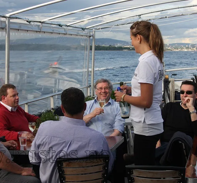 Servering av drikke til sittende gjester på båt med utsikt over fjorden.